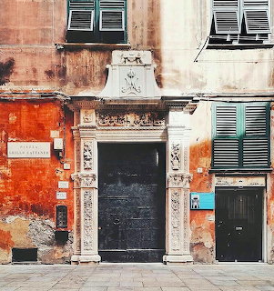 Weathered orange and cream building facade with ornate stone doorway and green shutters in historic Genoa plaza