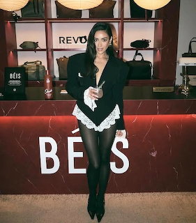 Woman in black blazer and boots posing at indoor event with illuminated backdrop