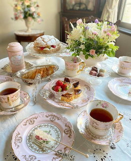 Afternoon tea table set with pink floral china, teacups, pastries, and flower arrangements