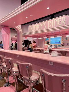 Pink retro diner interior with chrome bar stools, long counter, and neon Dunky's Diner sign