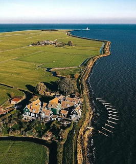 Aerial view of a coastal village with green fields and sea along a narrow shoreline