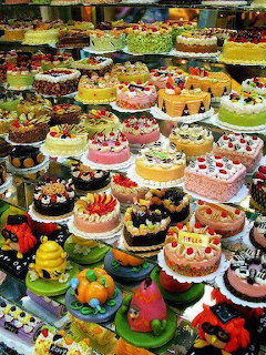 Multiple tiers of colorful decorated cakes with various frostings and toppings in a bakery display