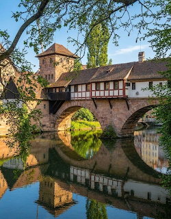 Historic half-timbered bridge and tower reflected in calm river, Nürnberg, Germany