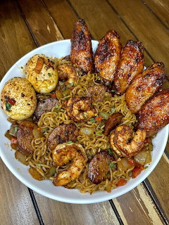 White bowl with ramen noodles, grilled shrimp, chicken wings, boiled eggs, and vegetables on a wooden surface