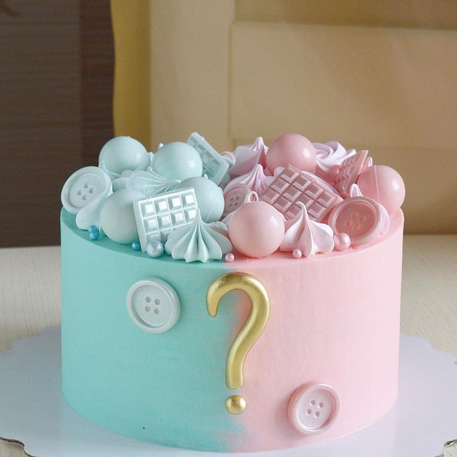 Split blue and pink cake with baby decorations and gold question mark on top