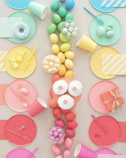 Pastel rainbow table setting with colorful plates, eggs, and utensils arranged in symmetrical rows