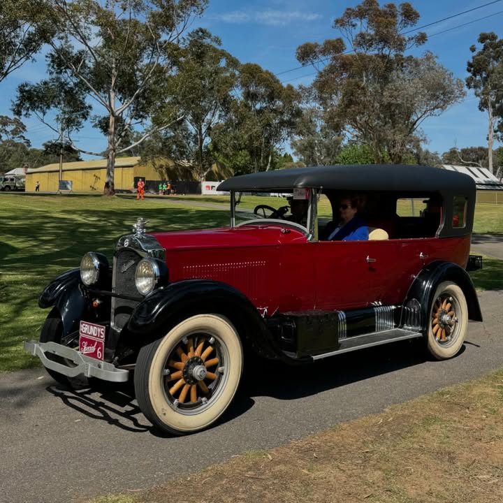 Red and black vintage car with whitewall tires parked on a road near trees and grass