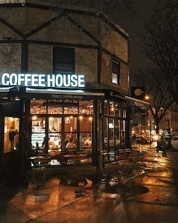 Coffee house with glowing windows and neon sign on a rainy night with wet reflective pavement
