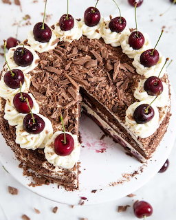 Black Forest cake with chocolate shavings, whipped cream, and cherries on white plate