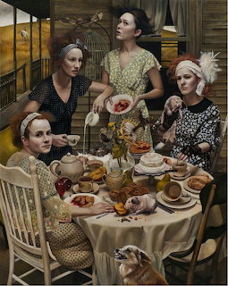 Four women in patterned dresses seated at table with tea and desserts in rustic room with autumn landscape beyond