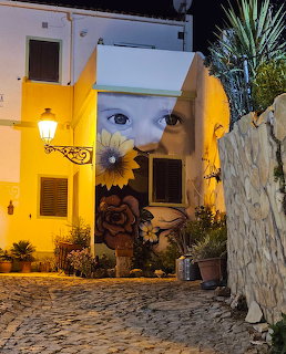 White building with yellow arch and large eye mural painting at night in Portuguese village