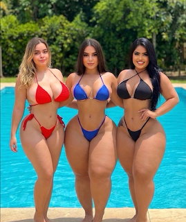 Three women in red, blue, and black bikinis posing together by a swimming pool