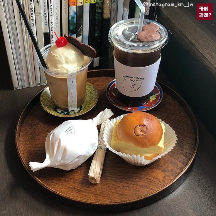 Tray with iced coffee, dessert drink, and pastries beside books near a window