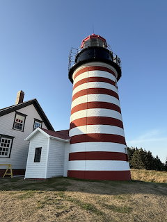 Red and white striped lighthouse with white keeper's house under blue sky