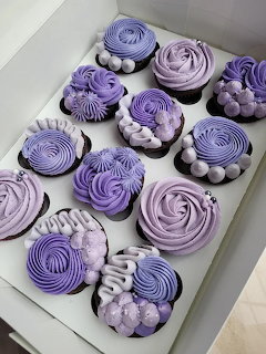 Box of cupcakes with purple and lavender frosting in decorative swirl and flower patterns