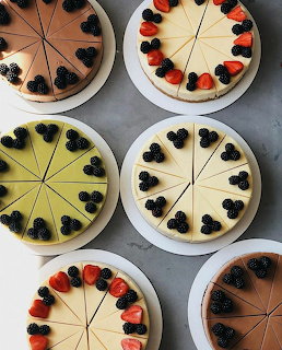 Six sliced cheesecakes on white plates seen from above, decorated with strawberries and blackberries