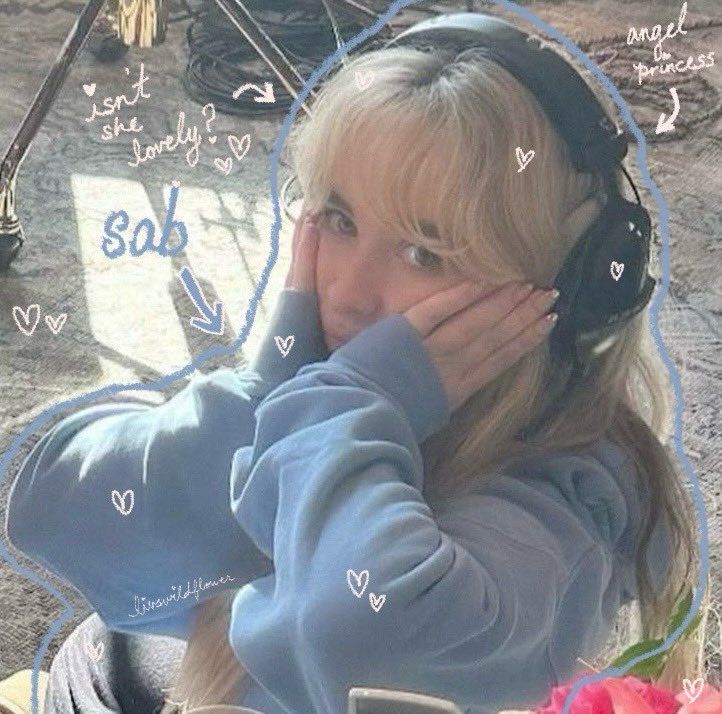 Blonde girl in a blue sweatshirt wearing black headphones, resting her face in her hands outdoors