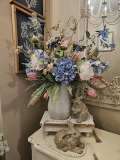 Spring flower arrangement with blue hydrangeas and pink tulips in a white vase next to a rabbit figurine