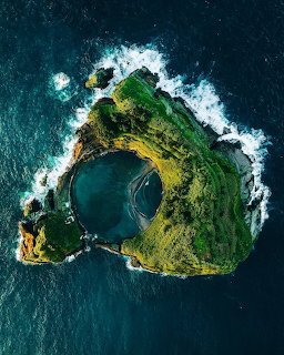 Aerial photograph of a small green volcanic island with a crater lake surrounded by blue ocean