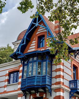 Colorful historic villa with orange striped facade, blue wooden balconies, and red tile roof framed by green foliage