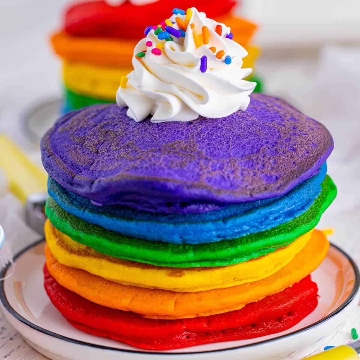 Stack of rainbow pancakes with whipped cream and sprinkles