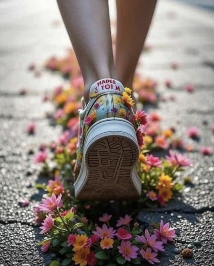 Person walking on pavement scattered with colorful flowers, view from behind showing shoe sole