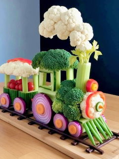 Train sculpture made from fresh vegetables with broccoli, celery, cauliflower clouds, and onion ring wheels
