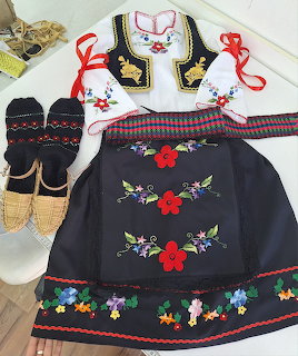 Serbian folk costume with embroidered vest, floral apron, and traditional accessories laid out on white surface