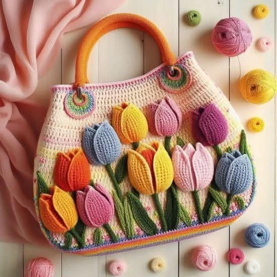 Handmade crochet bag with colorful 3D tulip flowers and wooden handles on white surface with yarn balls