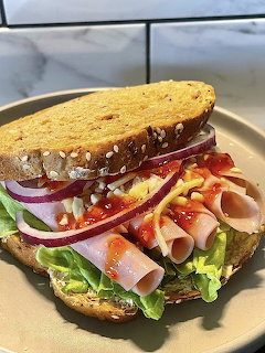 Thick deli sandwich with ham, vegetables, and wheat bread on a white plate