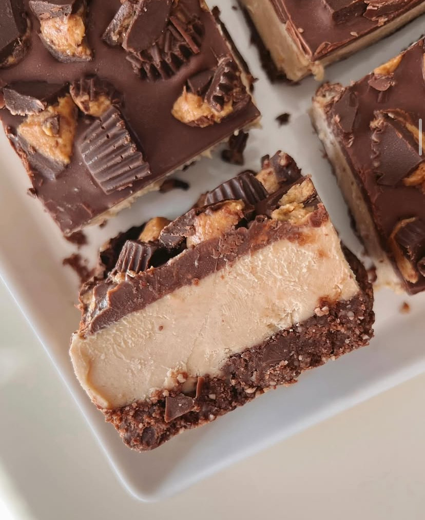 Layered peanut butter chocolate bars topped with mini peanut butter cups on a white plate
