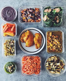 Meal prep containers with roasted chicken, vegetables, pasta, salad, and side dishes viewed from above