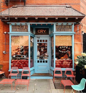 Blue cafe storefront with outdoor metal chairs and tables on sidewalk