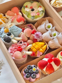 Box of assorted fruit tarts with berries, tropical fruit, and cream toppings arranged in compartments