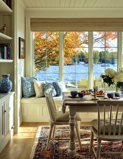 Cozy breakfast nook with window seat, rustic table, and autumn lake view through large windows