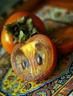 Two persimmons on a colorful patterned cloth, one cut open showing seeds and golden flesh