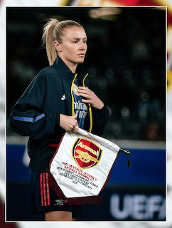 Leah Williamson holding an Arsenal pennant on a football pitch at a UEFA event