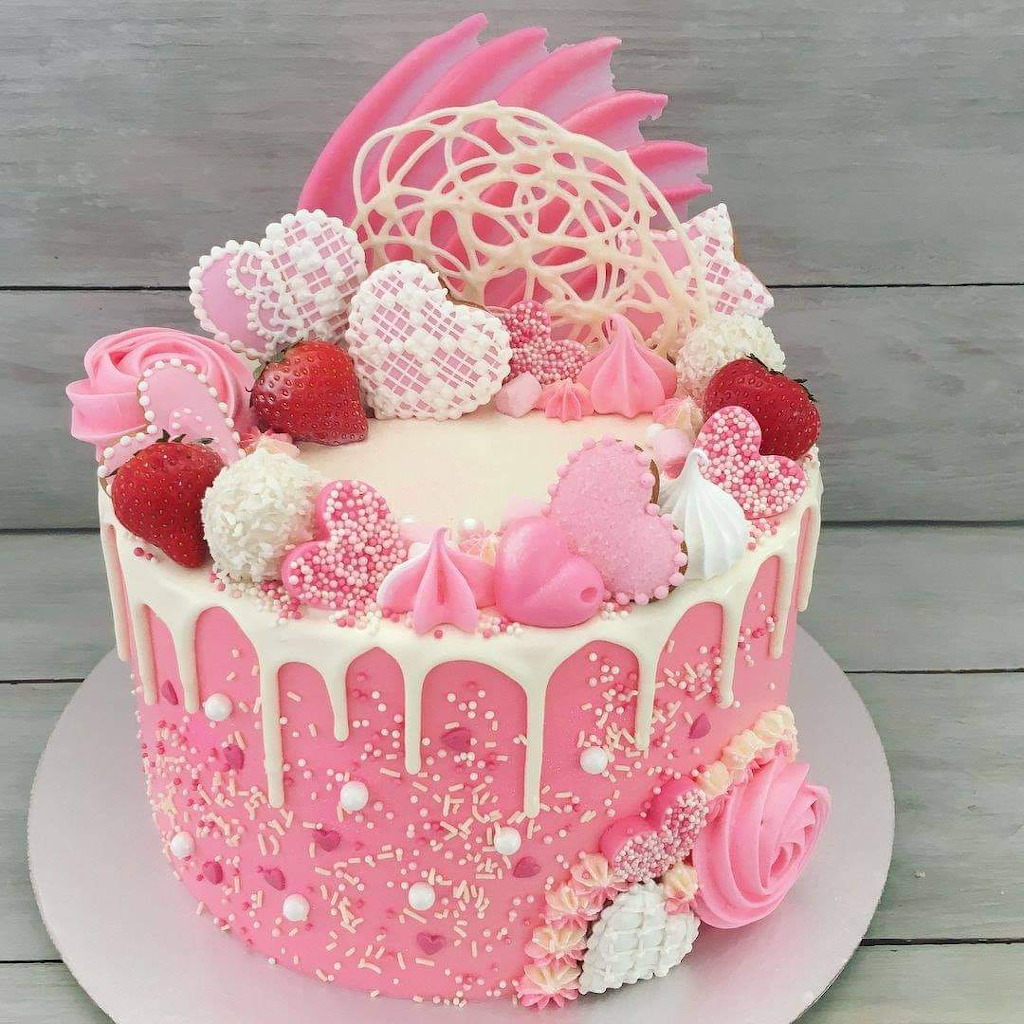 Pink frosted cake decorated with heart cookies, strawberries, meringues, and roses on wood surface
