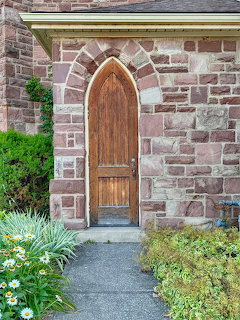 Arched wooden door in a stone building with a path and garden plants