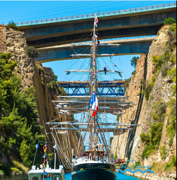 Tall ship sailing through narrow Corinth Canal with bridge above and steep cliffs on both sides