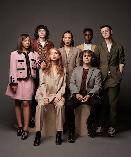 Six young adults posing in a studio portrait against a dark background.