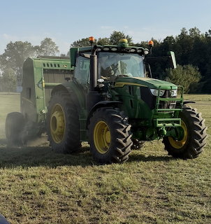 Green John Deere tractor with a round baler driving through a dry field