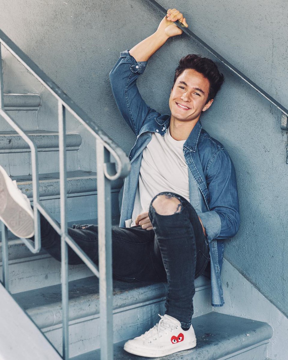Young man in denim jacket sitting on stairs smiling at camera