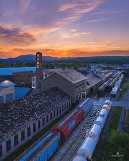 Aerial view of train yard with freight cars beside old industrial buildings at sunset with mountains