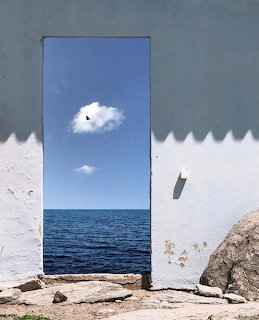 Doorway in a white wall framing the blue sea and sky with rocks in front