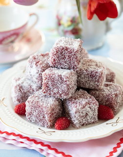 Stack of coconut-dusted cake cubes with jam filling and fresh raspberries on white plate