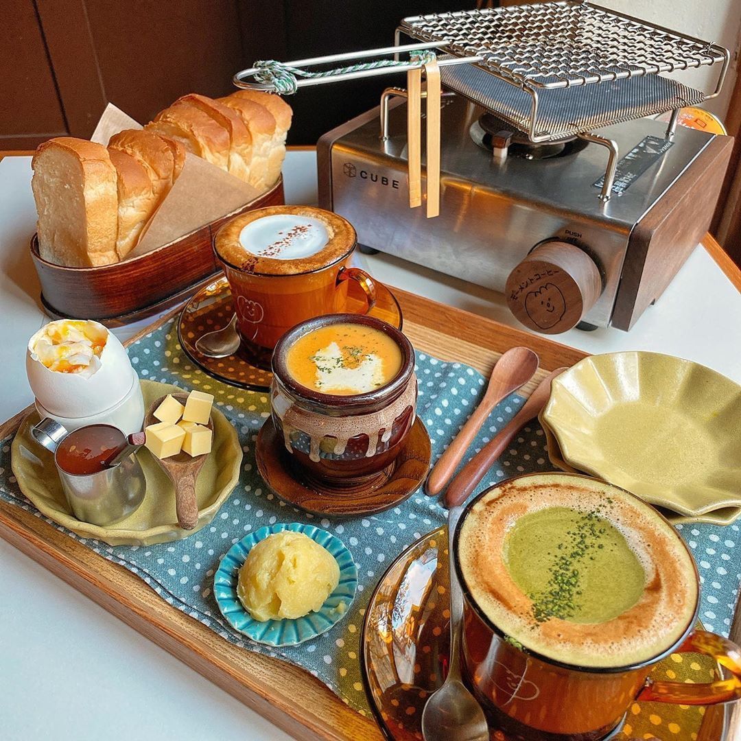 Japanese breakfast tray with grilled fish, soup, bread, tea, and various side dishes on a wooden tray