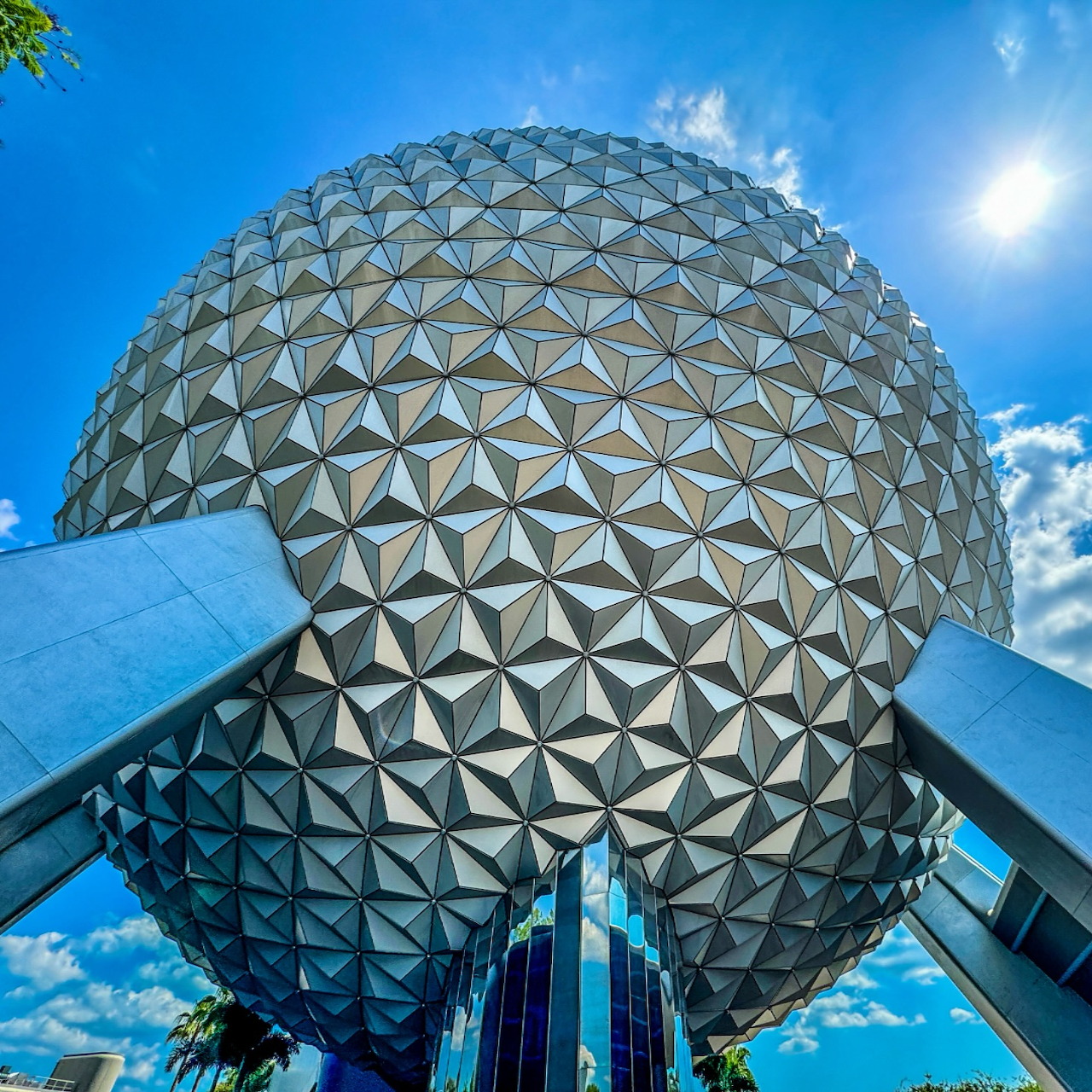 Silver geodesic sphere dome of Spaceship Earth at EPCOT against blue sky with sun
