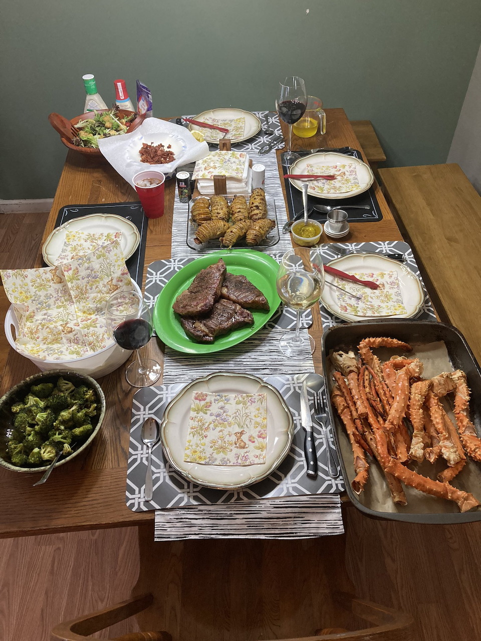 Overhead view of a dining table with crab legs, grilled meat, soup, greens, and flatbreads