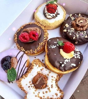 Five decorated dessert tarts with chocolate, strawberries, and various toppings on white plate